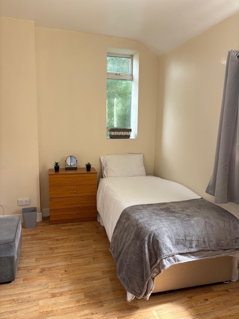 A single bedroom with natural light from the window and a made bed